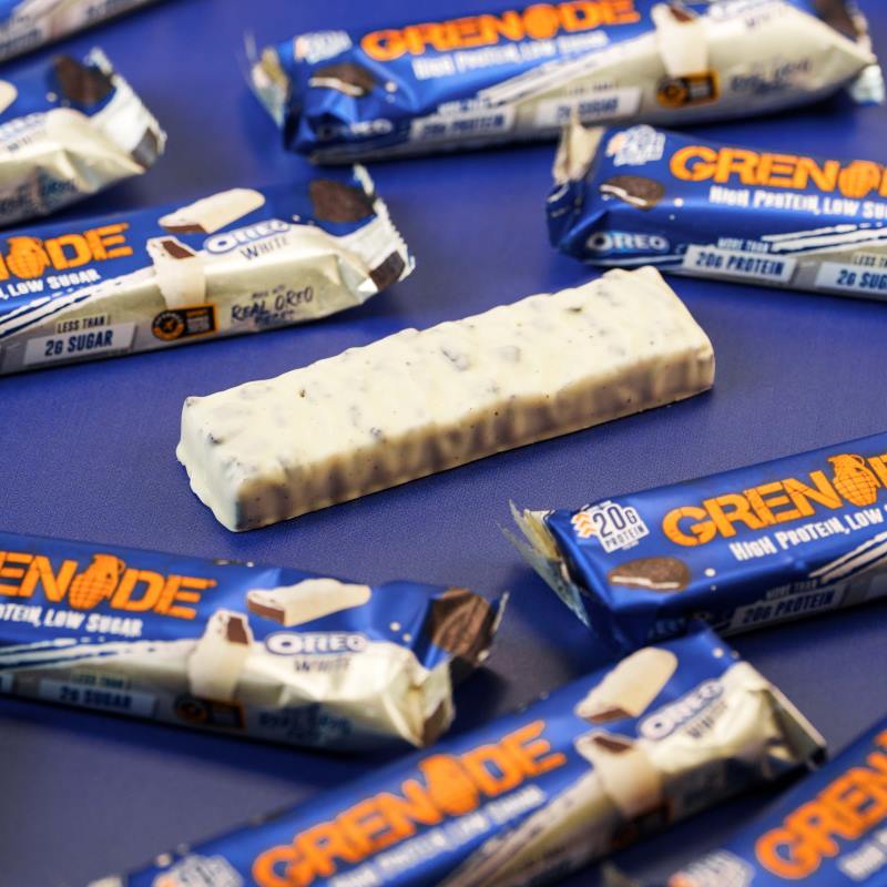 Grenade Proteinriegel Oreo White liegt auf einem Tisch – Proteinreicher, zuckerarmer Snack mit 20g Protein, umhüllt von weißer Schokolade und Oreo-Stückchen.