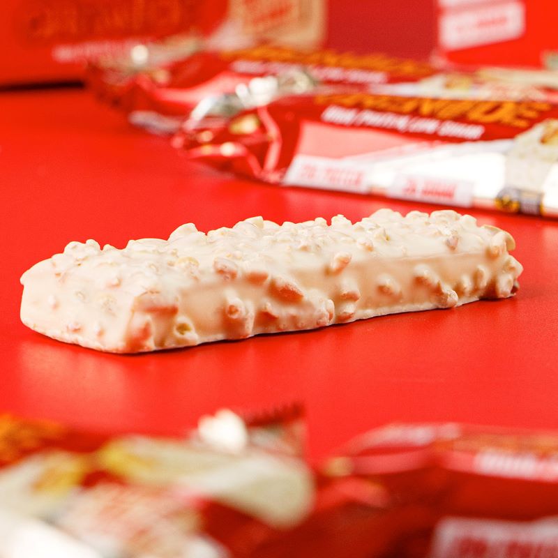 Grenade Protein Riegel White Chocolate Salted Peanut liegend auf einem Tisch, umhüllt von weißer Schokolade und Erdnussstückchen, mit 20g Protein und weniger als 2g Zucker pro Riegel.