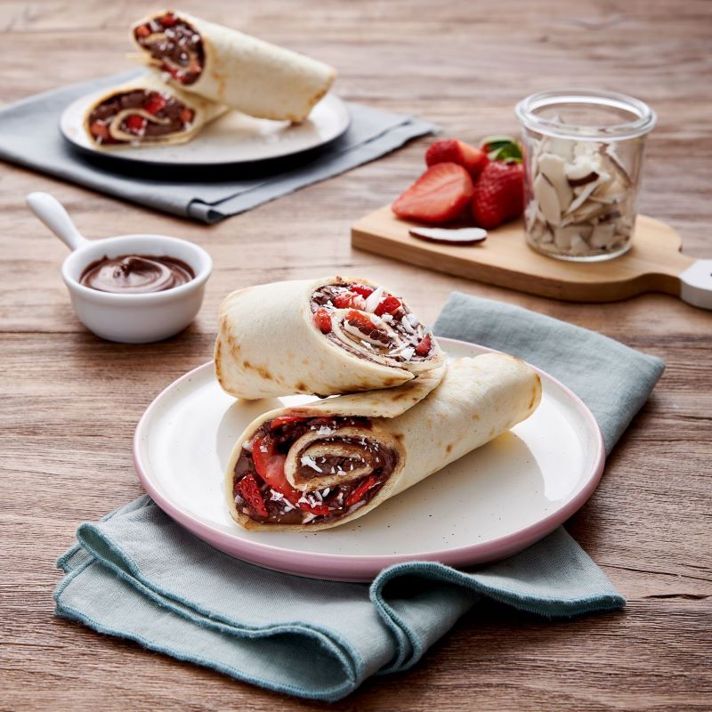 Gefüllter Loriana Piadina ARROTOLABILE OLIO Wrap mit Schokoladencreme und frischen Erdbeeren auf einem Tisch. Süße italienische Spezialität.